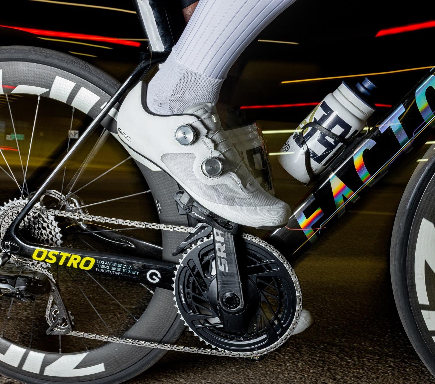 Ciclista de carretera con zapatillas de ciclismo blancas Giro enganchadas al pedal de una bicicleta Factor Ostro con bielas SRAM y rueda de carbono