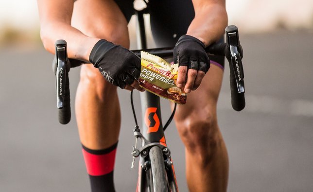 A biker opens a bag of fruit gummies while riding.