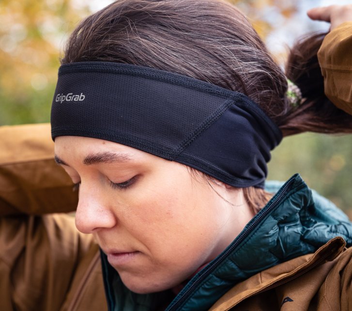 A young woman in a sand-coloured rain jacket pulls her ponytail through a black headband.