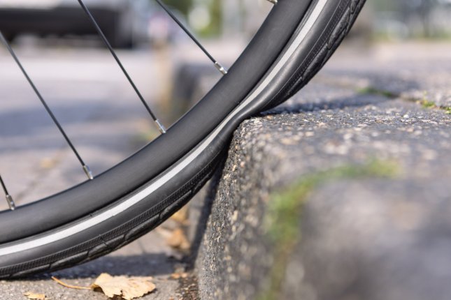 Close-up photo: A bicycle tyre is compressed flat against a kerb all the way to the rim.