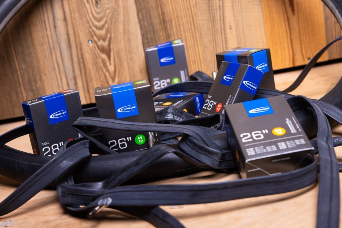 Some empty black rubber bicycle tubes lie tangled on a wooden surface. In between are grey-silver Schwalbe boxes containing tubes.