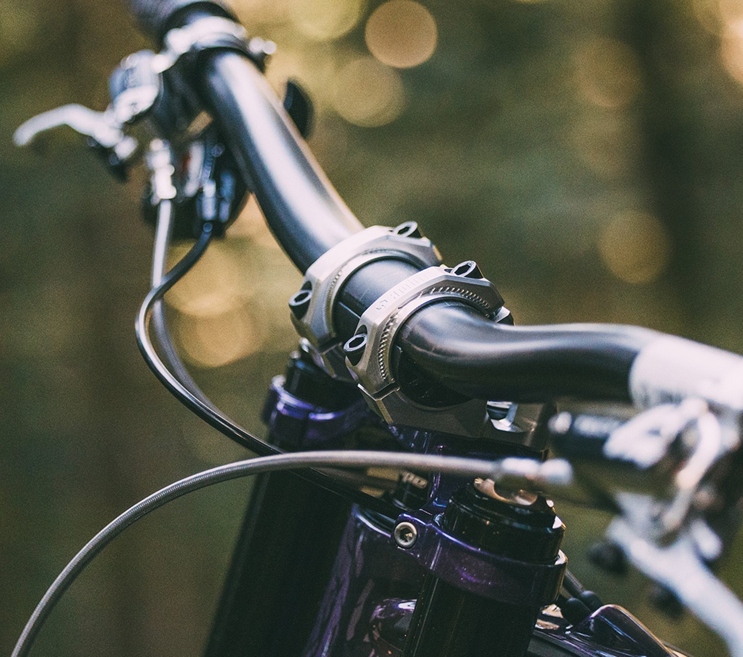 Mountainbiker mit Fullface-Helm steht mit seinem Bike im moosbedeckten Wald, Detailaufnahme vom Ambit Handlebar Lenker für maximale Kontrolle im Trail, Sonnenlicht scheint durch die Bäume