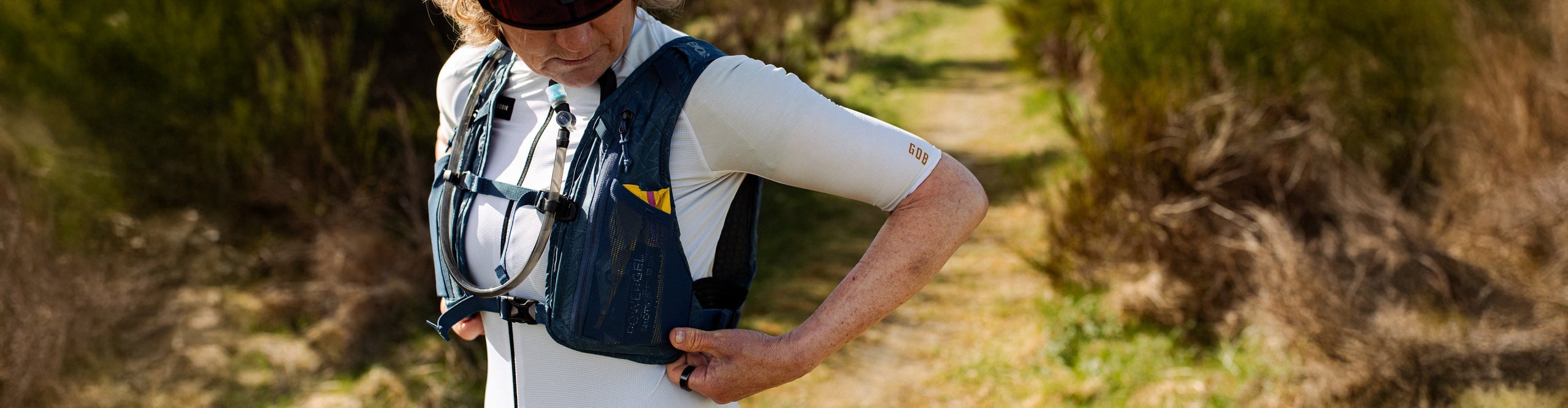 Gravel-Bikerin mit Helm und Sonnenbrille justiert ihre Trinkweste auf naturbelassenem Trail – funktionale Ausrüstung für lange Touren
