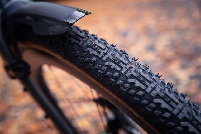 Detail shot: a gravel tyre tread with autumn leaves softly blurred in the background.