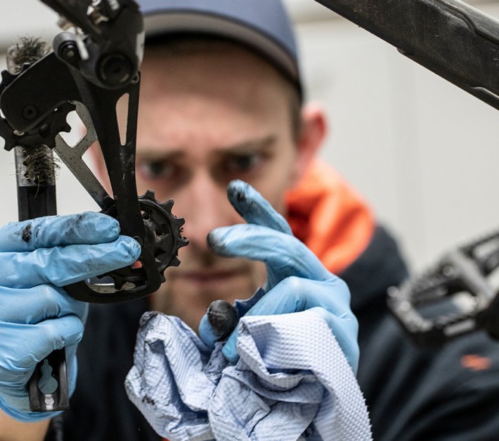 bc-Mechaniker Thomas reinigt das untere Schaltröllchen des Schaltwerks mit einem blauen Papiertuch.