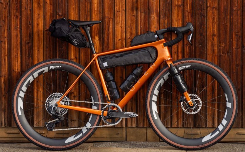 Orange OPEN U.P. gravel bike with Adventure fork, bikepacking bags and Zipp wheels in front of a wooden wall.