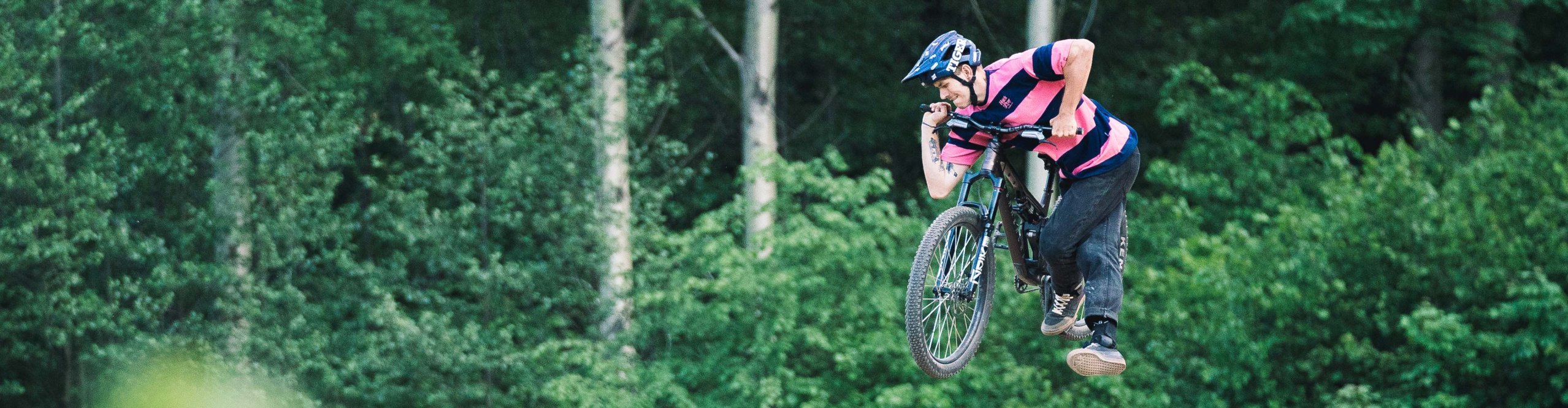 Mountain biker wearing Loose Riders apparel performing a jump on a trail mountain bike in the forest