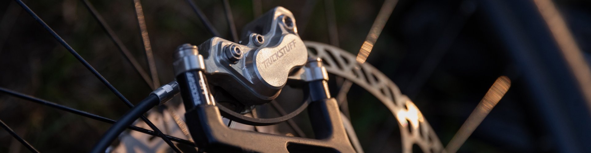 Close-up of a Trickstuff bike component on a mountain bike wheel with a brake disc, illuminated by warm light.
