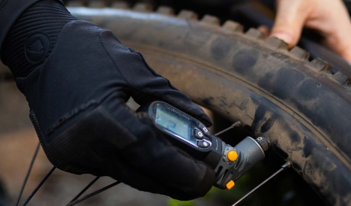 Ciclista de montaña midiendo la presión de un neumático de MTB con tacos usando un medidor digital.