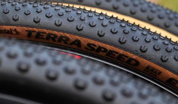 Gros plan de plusieurs pneus de gravel avec profil marqué et flancs beiges, superposés, mettant en avant la structure et la bande de roulement.