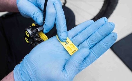 Ein gelber Abstandshalter für hydraulische Magura-Fahrradscheibenbremsen liegt auf einer Hand mit blauen Handschuhen.