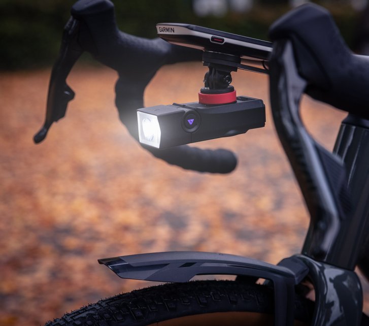 A bicycle front light is mounted hanging below the bike computer on the cockpit of a gravel bike.