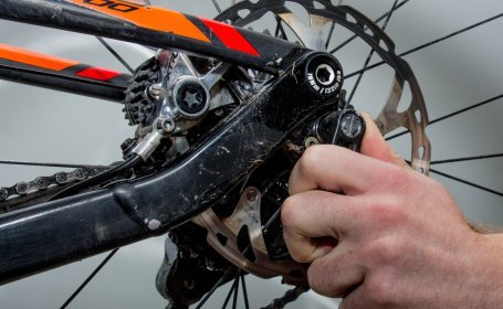 Gros plan sur un frein à disque de vélo tandis qu’une main resserre ou desserre la vis de fixation de l’étrier.