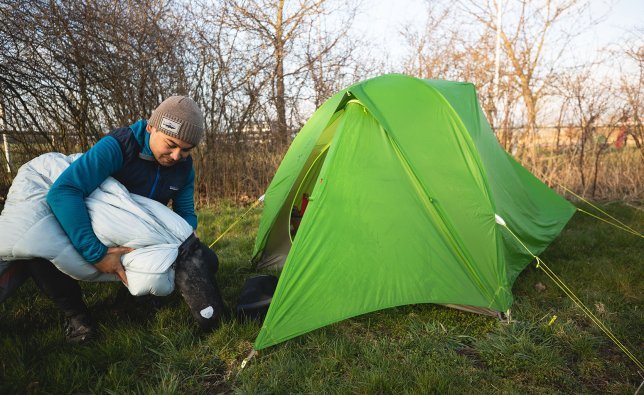 Marcel from bc Marketing stuffs his sleeping bag into its stuff sack. He is kneeling in front of the entrance of his tent.