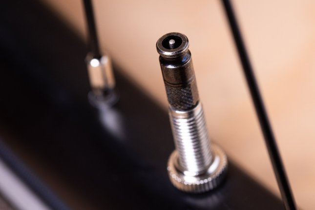 Close-up: A Schwalbe Clik Valve mounted on a bicycle, seen from above. The small pin in the center of the metallic black valve head is visible.