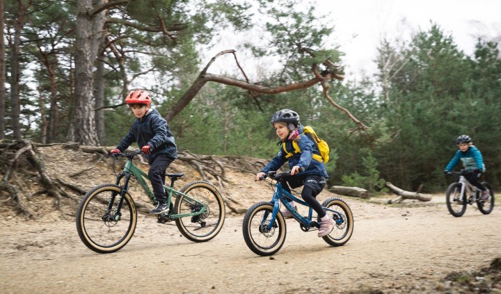 Tres niños en bicis de montaña para SUPURB y Specialized por un sendero forestal.