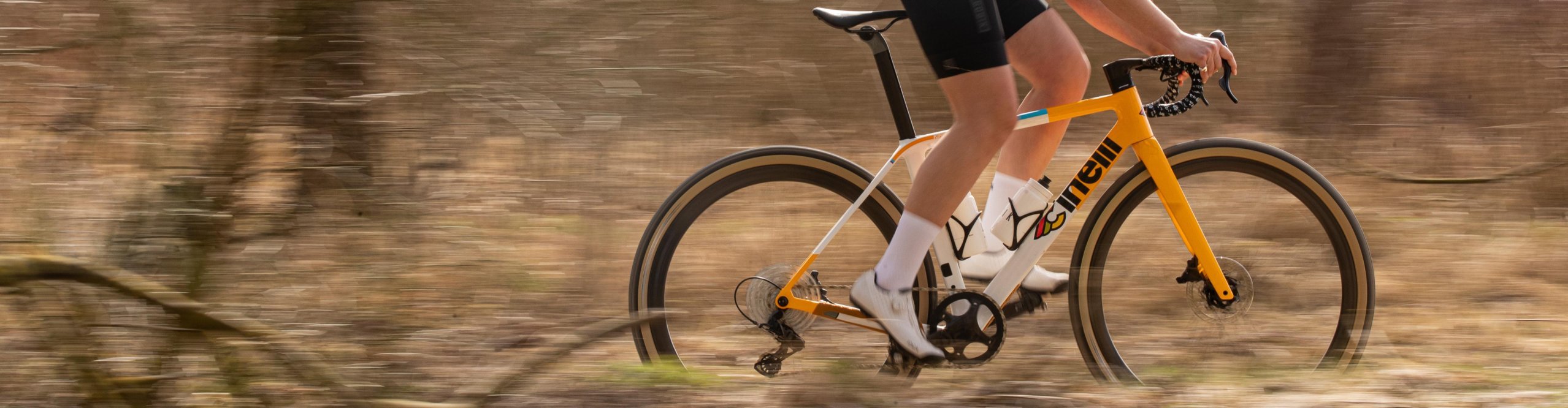 Fahrerin auf einem gelben Cinelli Zydeco II Gravelbike fährt dynamisch durch einen herbstlichen Wald, der Hintergrund ist in Bewegungsunschärfe.