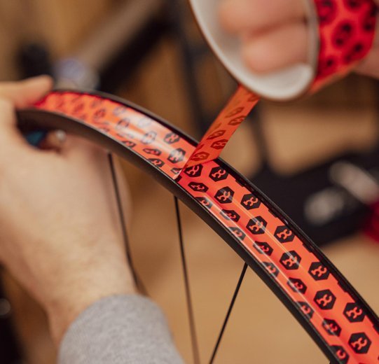 Main posant un fond de jante sous tension dans une jante de vélo, avec plusieurs centimètres de chevauchement.