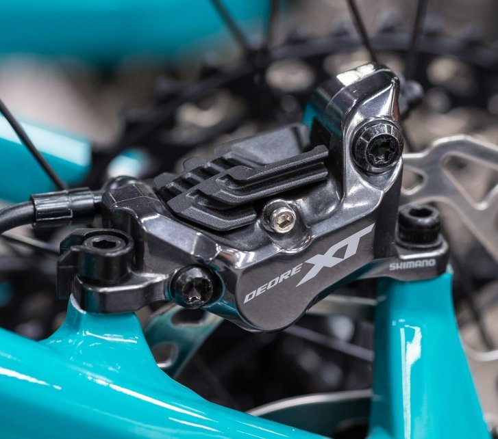 Gros plan sur un étrier de frein à disque Shimano Deore XT monté sur un cadre de vélo turquoise.