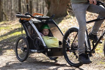 Toddler sitting safely in a bike trailer wearing a helmet while being towed along a forest path.