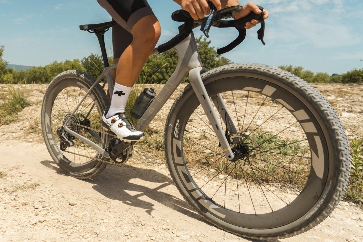 Gravel cyclist rides an OPEN WI.DE with wide tires and aero wheels on a dusty gravel road.