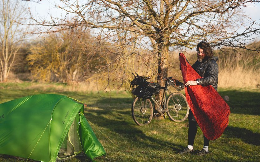 Christian, du service clientèle de bc, replie son matelas de camping. Au premier plan se trouve sa tente, à l'arrière-plan son vélo.