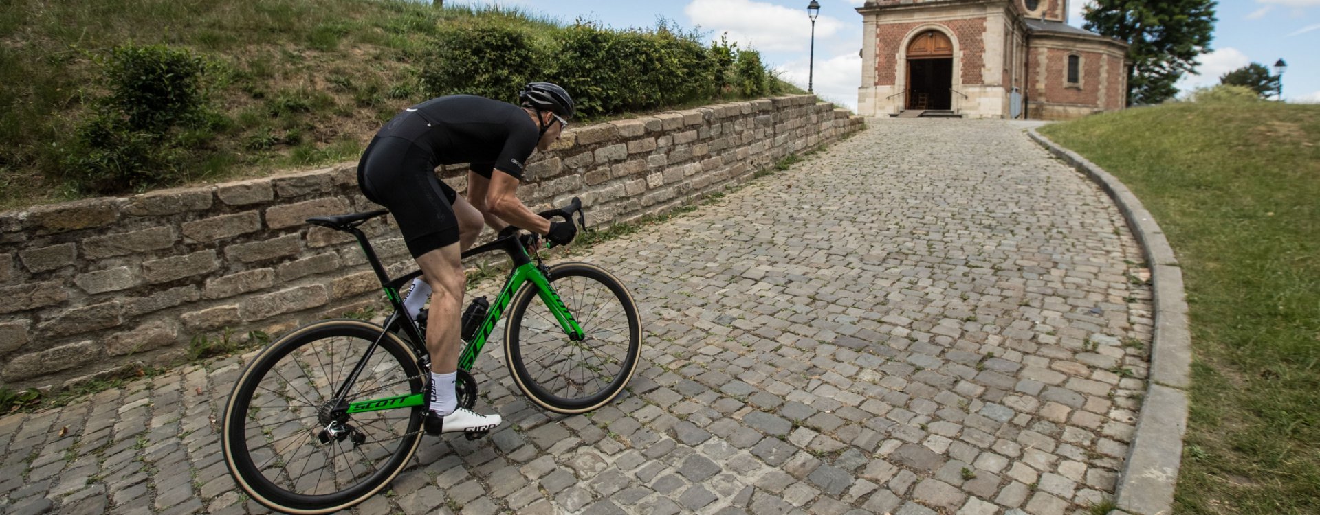 A road cyclist sprints up a hill. He’s riding over cobblestones.