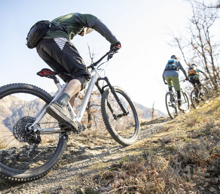 A group of mountain bikers ride up a rocky climb in sunny weather.