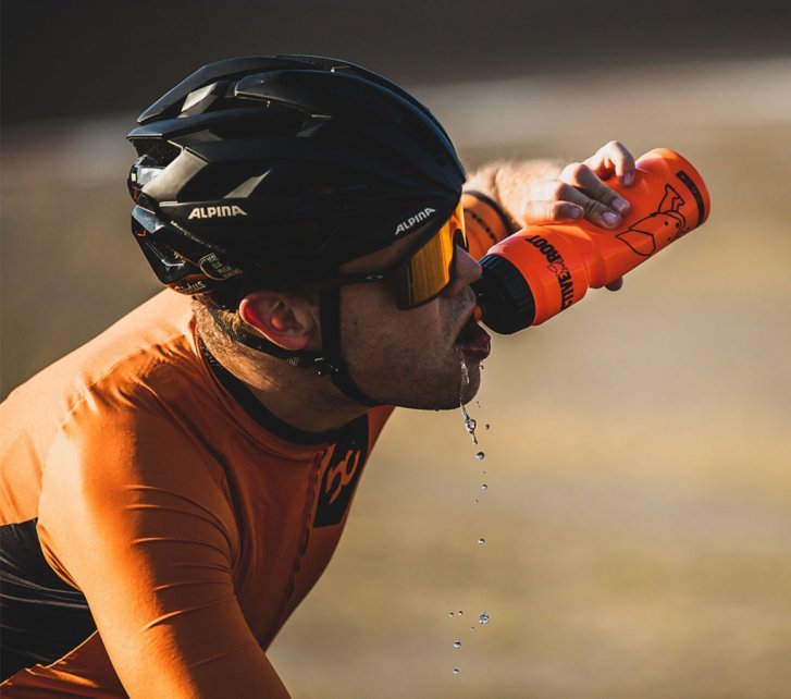 Un ciclista bebe un gran trago de un bidón.