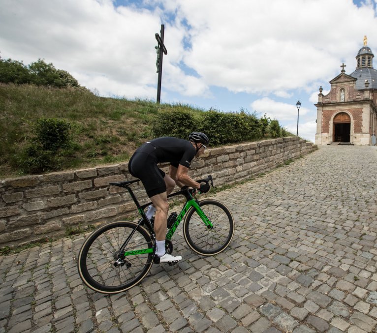 A road cyclist sprints up a hill. He’s riding over cobblestones.