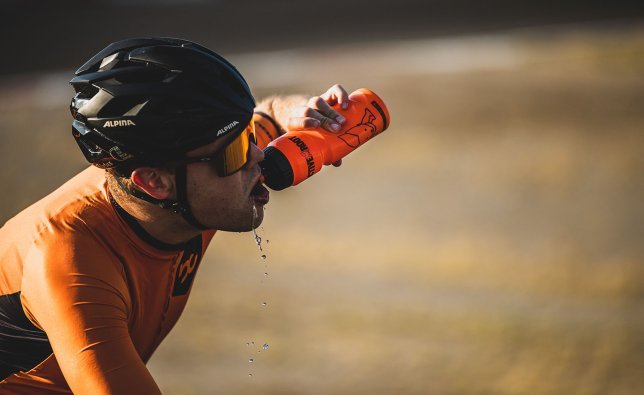 Un ciclista bebe un gran trago de un bidón.