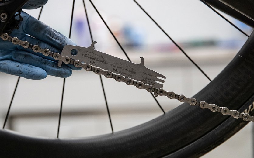 Utilizando un medidor de desgaste de cadena para determinar el estado de la cadena de una bicicleta de ruta. 